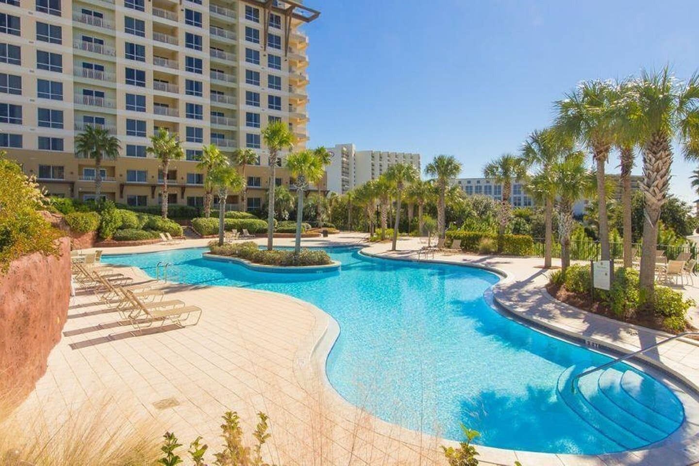 Un hotel con una gran piscina rodeada de palmeras y sillas de descanso.