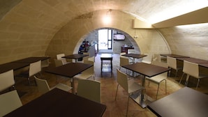 A dining area with tables and chairs, a central island, and a stone archway leading to an outdoor area. - Vista Sui Sassi (Matera)