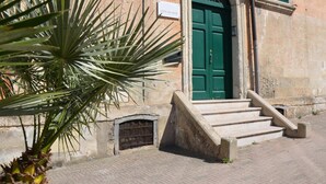 A building with a green door, a small staircase leading to the entrance, and a palm tree in the foreground. - Vista Sui Sassi (Matera)