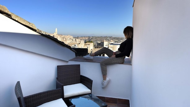 A balcony with a view of a cityscape, wicker furniture, and a glass table. - Vista Sui Sassi (Matera)