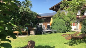 Un jardin avec une terrasse en bois, un barbecue et un espace détente avec des fauteuils.
