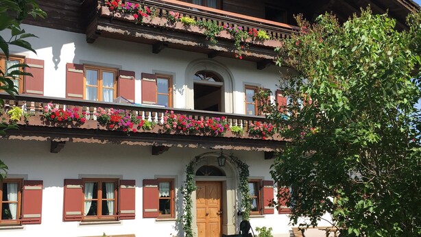 Un chalet traditionnel doté d’un balcon agrémenté de fleurs, d’un banc en bois et d’une balançoire.