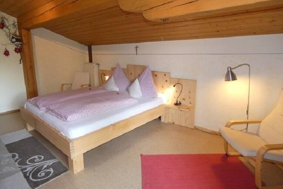 A wooden-framed bed with a headboard, two bedside tables with lamps, a chair, and a red rug.