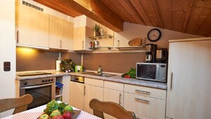 Une cuisine compacte équipée d’une cuisinière, d’un four, d’un four à micro-ondes et d’un évier. Il y a une horloge au mur et une petite plante sur l’étagère.