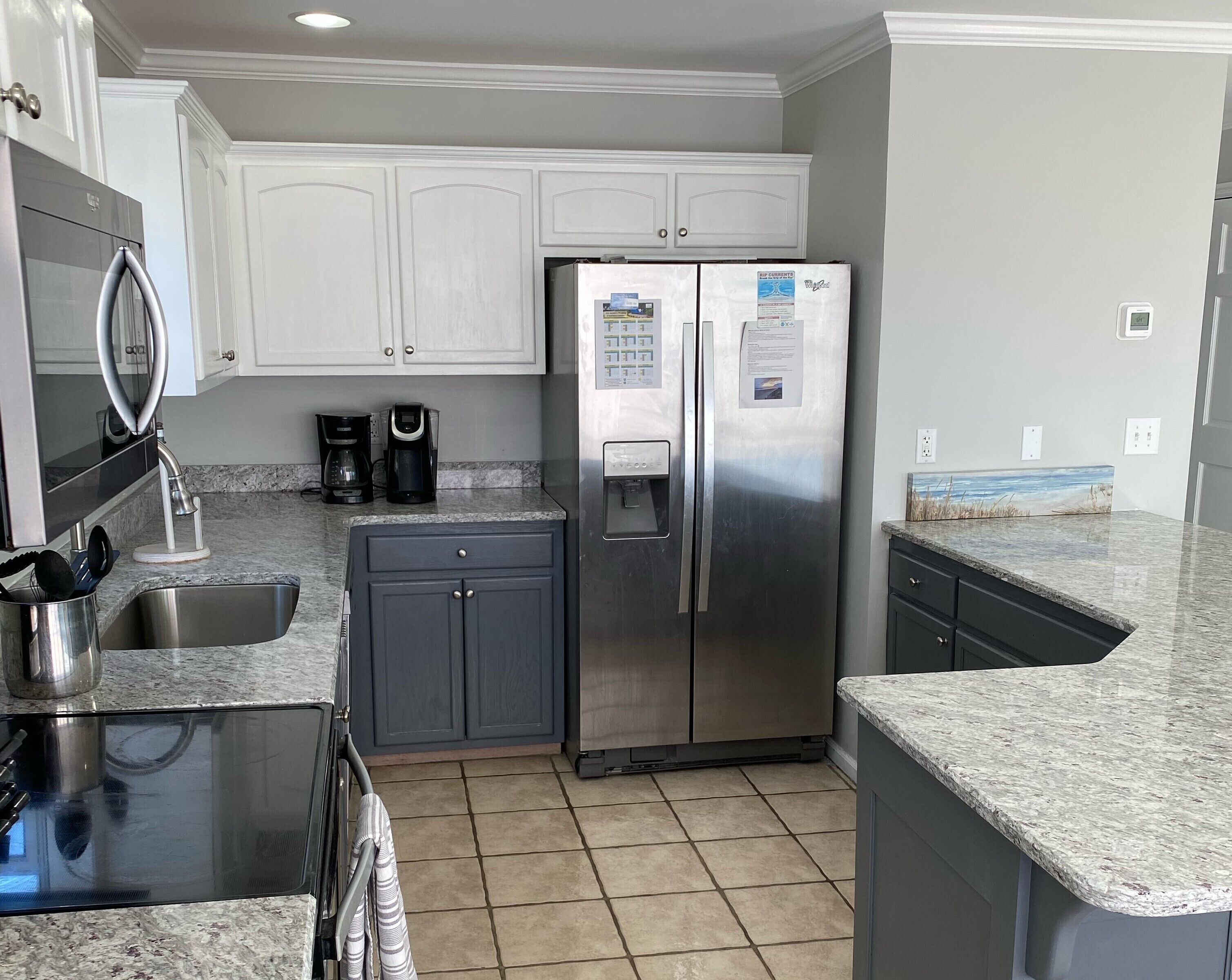 A modern kitchen with white cabinets, a stainless steel refrigerator, a built-in oven, and a granite countertop.