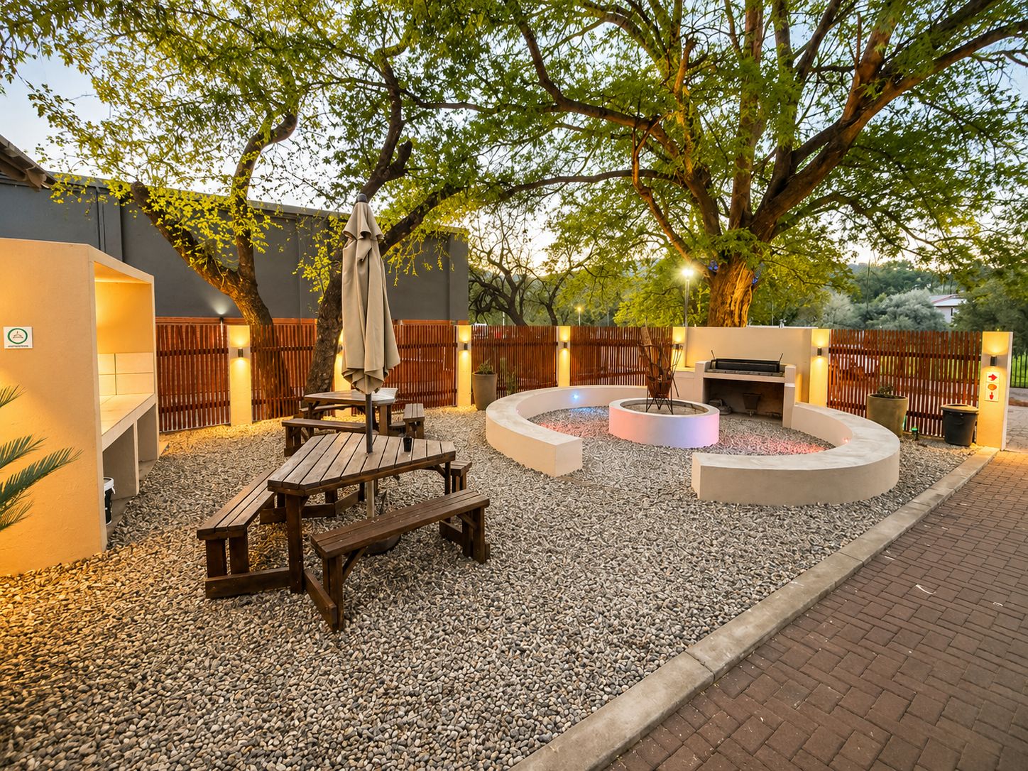 Un patio exterior con un conjunto de asientos circulares, una parrilla de barbacoa y un árbol que da sombra.