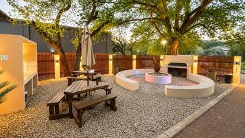 Un patio exterior con un conjunto de asientos circulares, una parrilla de barbacoa y un árbol que da sombra.