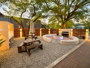 An outdoor patio area with a circular seating arrangement, a barbecue grill, and a tree providing shade.