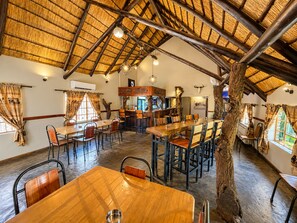 A rustic dining area with wooden tables and chairs, a thatched roof ceiling, and a central bar area. - Echo Mountain Inn (Thabazimbi)