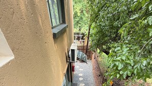 Una escalera conduce a un espacio exterior cubierto con vistas a un jardín y un edificio de fachada color crema.