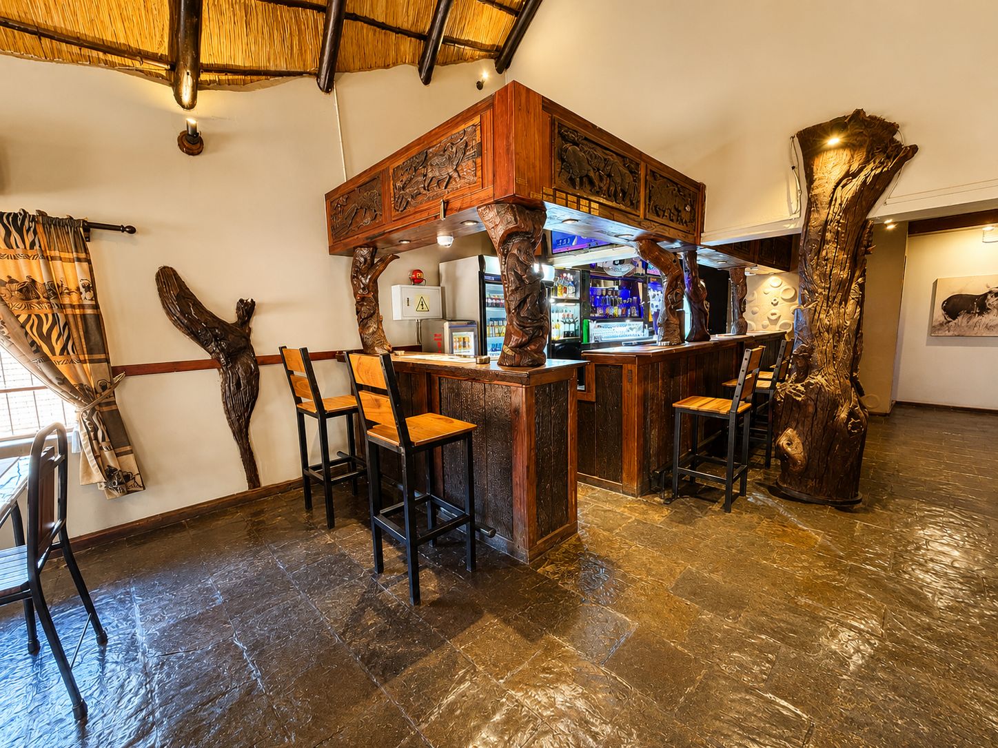 Un espace bar doté de tabourets et d’un comptoir en bois, le tout agrémenté de décorations sculptées en bois.