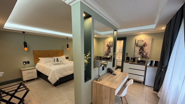 Una habitación de hotel moderna con cama, escritorio, espejo y kitchenette.