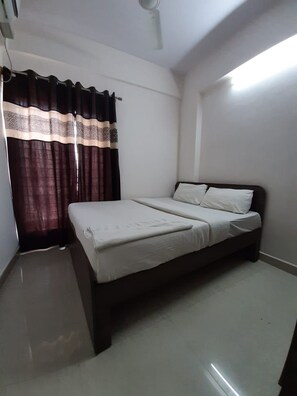 Una cama individual con ropa de cama blanca en una habitación con paredes blancas y suelo oscuro.