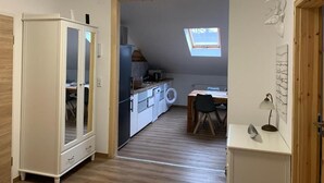 Une cuisine compacte dotée d’un puits de lumière, un coin repas avec une table et des chaises, et une armoire blanche.