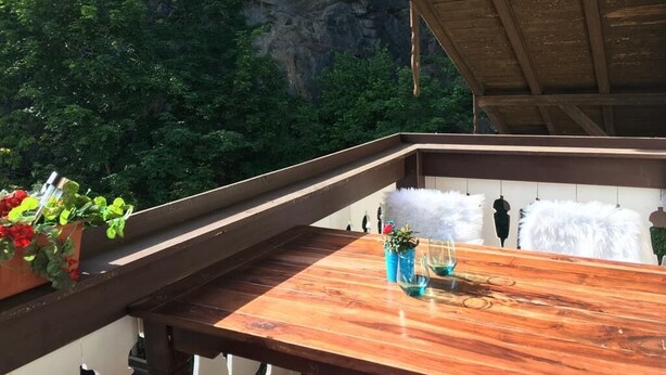 Un balcon en bois offrant une vue sur une falaise rocheuse et une végétation luxuriante.