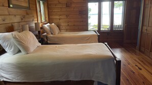 Een kamer in chaletstijl met twee bedden, houten wanden, een raam met uitzicht en een ingelijst schilderij aan de muur.