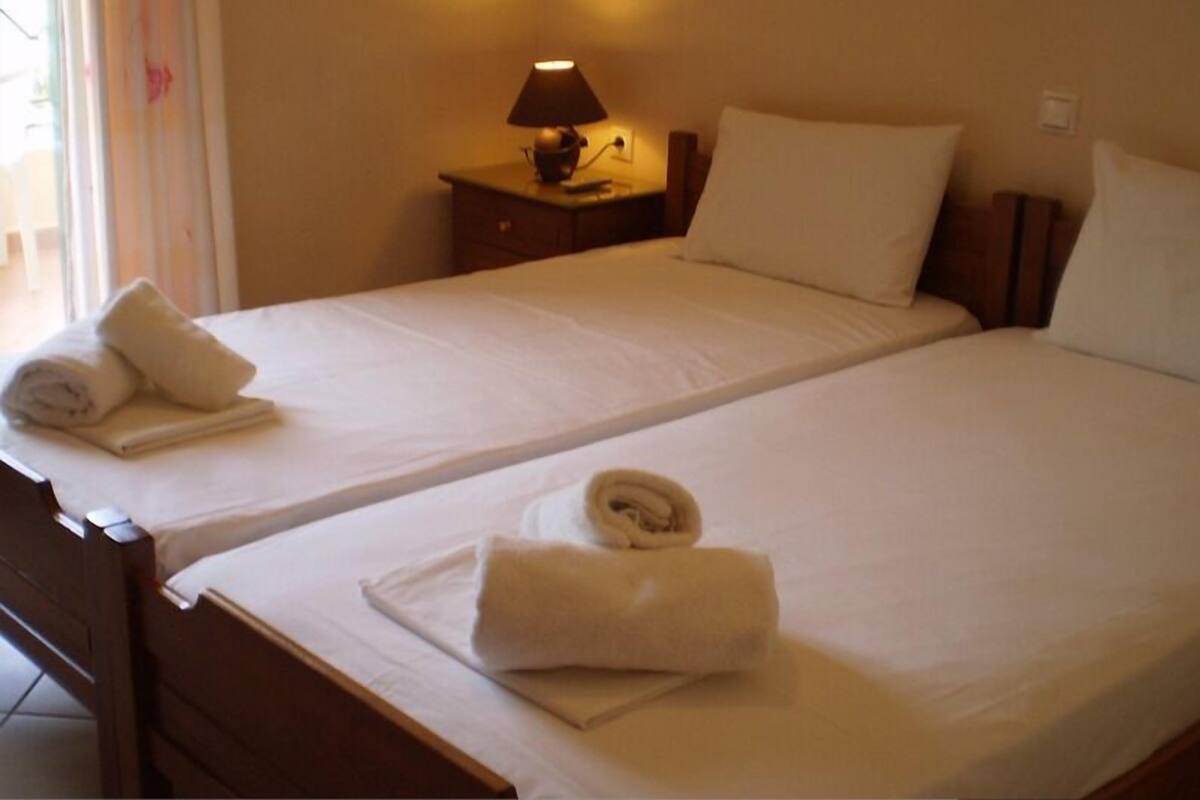 A hotel room with two single beds, each with a rolled towel and a nightstand with a lamp.