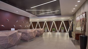 A modern reception area with geometric-patterned reception desks, recessed lighting, and a large abstract painting on the wall.