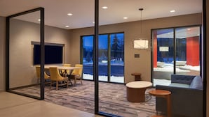 A modern hotel room with a large sliding glass door leading to a snowy outdoor area, a dining area with yellow chairs, and a cozy seating area with a blue sofa and a round table.