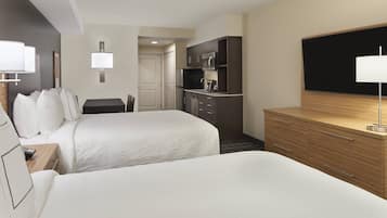 Ett hotellrum med två sängar, ett litet kök, en TV och ett skrivbord.