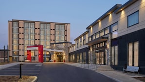 A modern hotel entrance with a red and beige facade, a covered driveway, and a parking area.