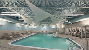 An indoor swimming pool with a high ceiling, lounge chairs, and exercise equipment.
