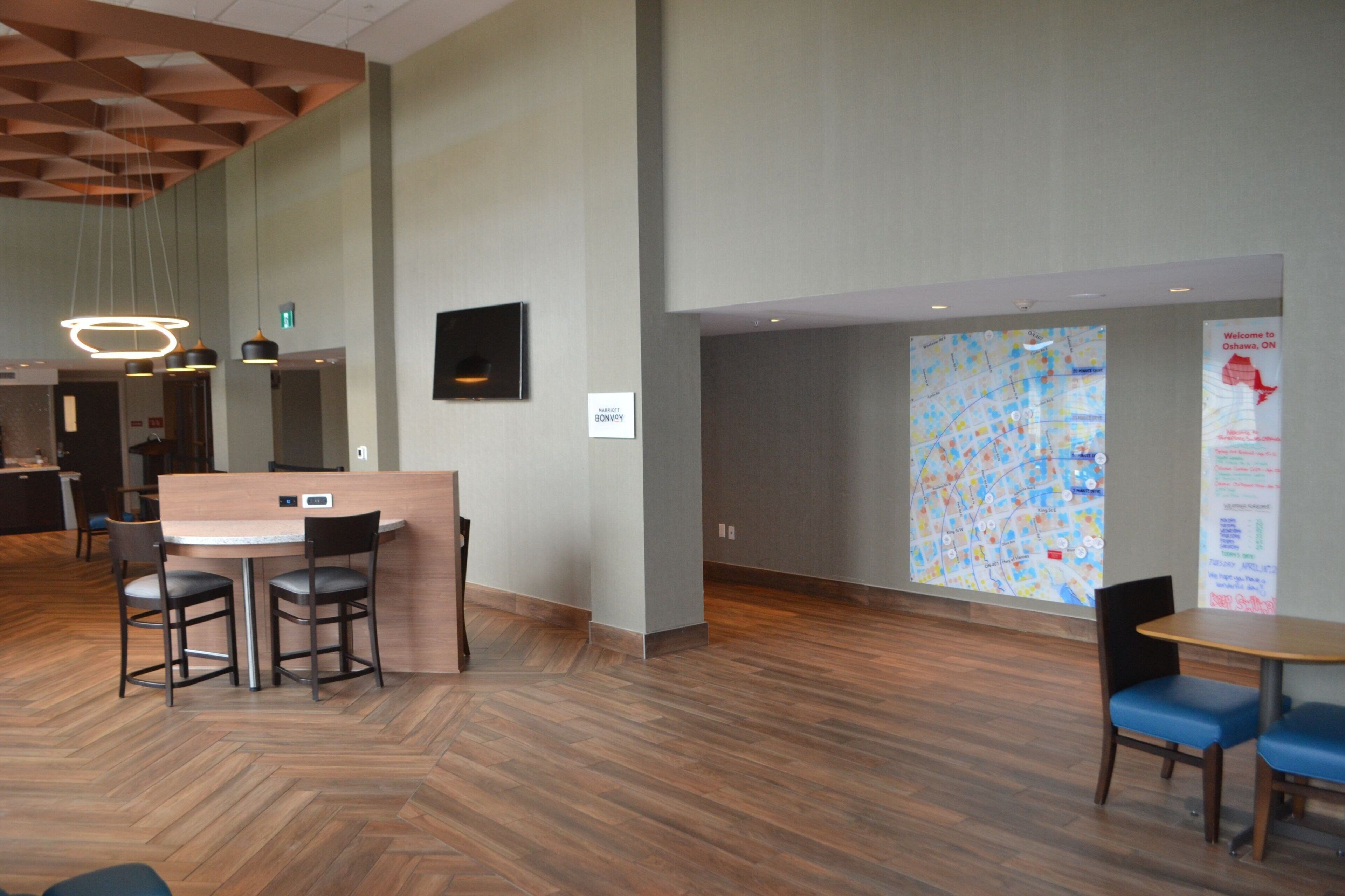 A modern hotel lobby with a wooden herringbone floor, a reception desk, and a large map display on the wall.