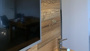Ein modernes Zimmer mit großem Flachbildfernseher an einer Holzwand, einem Holztisch mit Stühlen und einer aufgehängten Geweihdeko.