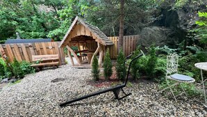 Eine rustikale Holzkonstruktion mit dem Schild 'Schweizerhaus - Dresden' in einem Garten mit Kies, einer Bank und einem Metallstuhl.