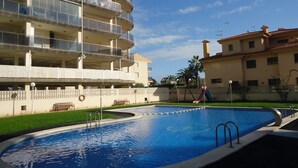 A swimming pool with a surrounding fence, a children's play area, and a multi-story building with balconies. - P. Maritimo 40 Lateral LEK (Peñiscola)