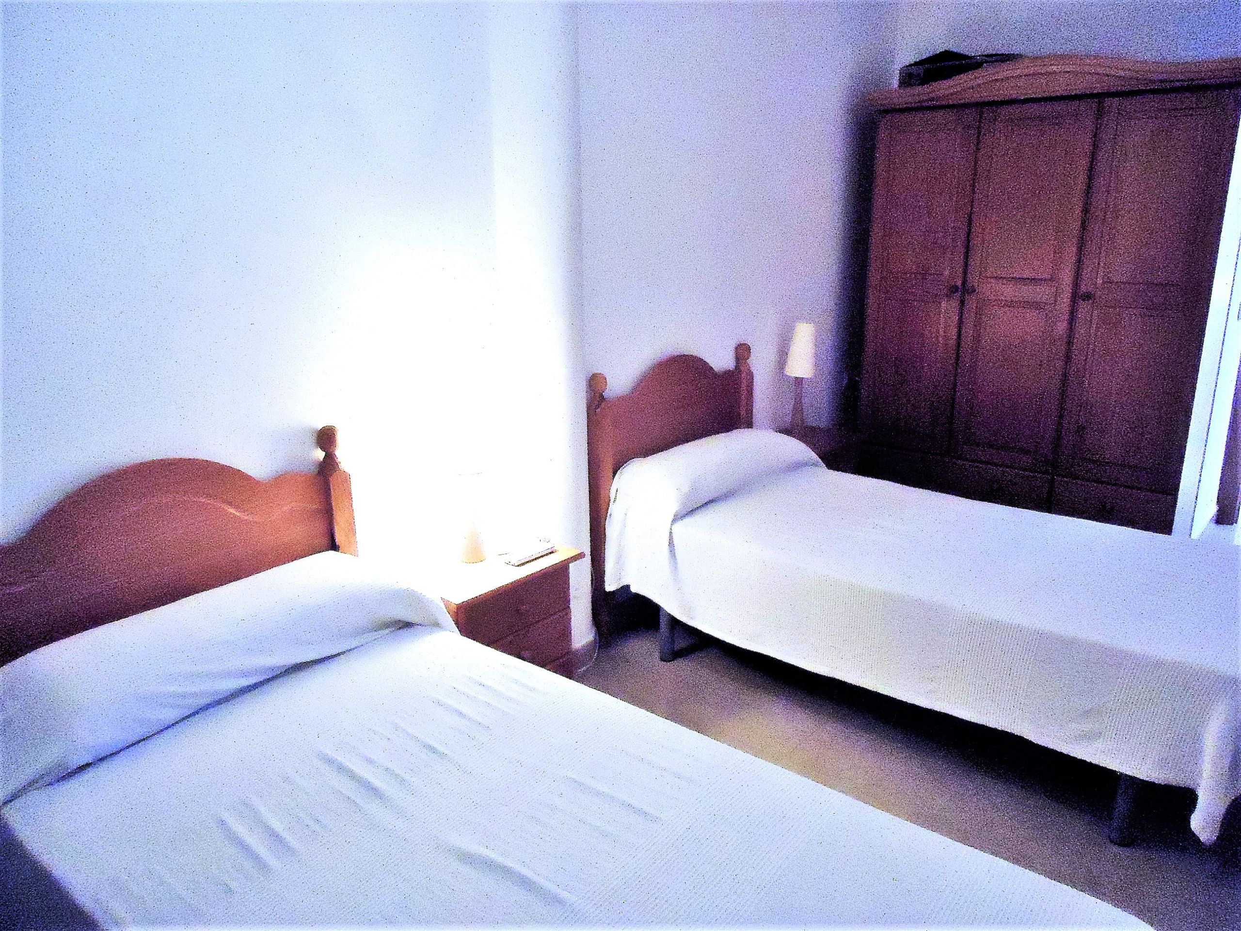 Una habitación con dos camas individuales, un armario de madera y una mesita de noche con lámpara.