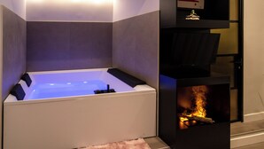 A modern bathroom with a built-in bathtub, a fireplace, and a shelf with a decorative item. - VESUVIANUS Rooms and More (Naples)