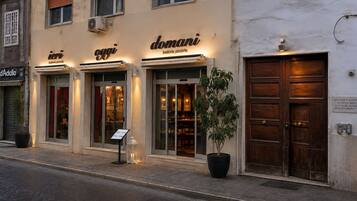 A building with three storefronts, each with a sign indicating a trattoria pizzeria. There is a potted plant in front of the middle storefront.