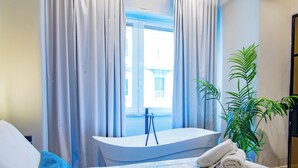 A hotel room with a bed, a window with curtains, a bathtub, and a potted plant. - VESUVIANUS Rooms and More (Naples)