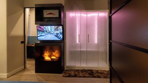 A modern living room with a fireplace, a television mounted on a black stand, and a white wardrobe with sliding doors. - VESUVIANUS Rooms and More (Naples)
