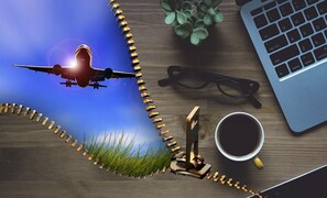 Ein Schreibtisch mit einem Laptop, Brille, Kaffeetasse, Pflanze und einem Modellflugzeug.