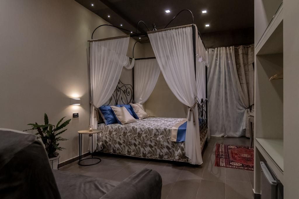 Une chambre à coucher avec un lit à baldaquin, une table de chevet, une plante en pot et un tapis rouge à motifs.
