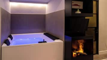 A modern bathroom with a built-in bathtub, a fireplace, and a shelf with a decorative item.