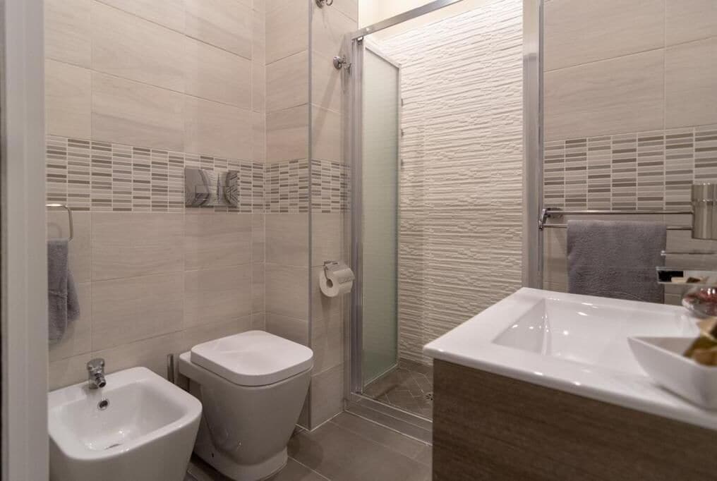 Uma casa de banho moderna com cabine de duche em vidro, bidé, sanita e lavatório com espelho.