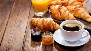 En frukostuppdukning med croissanter, apelsinjuice, kaffe och marmelad på ett träbord.