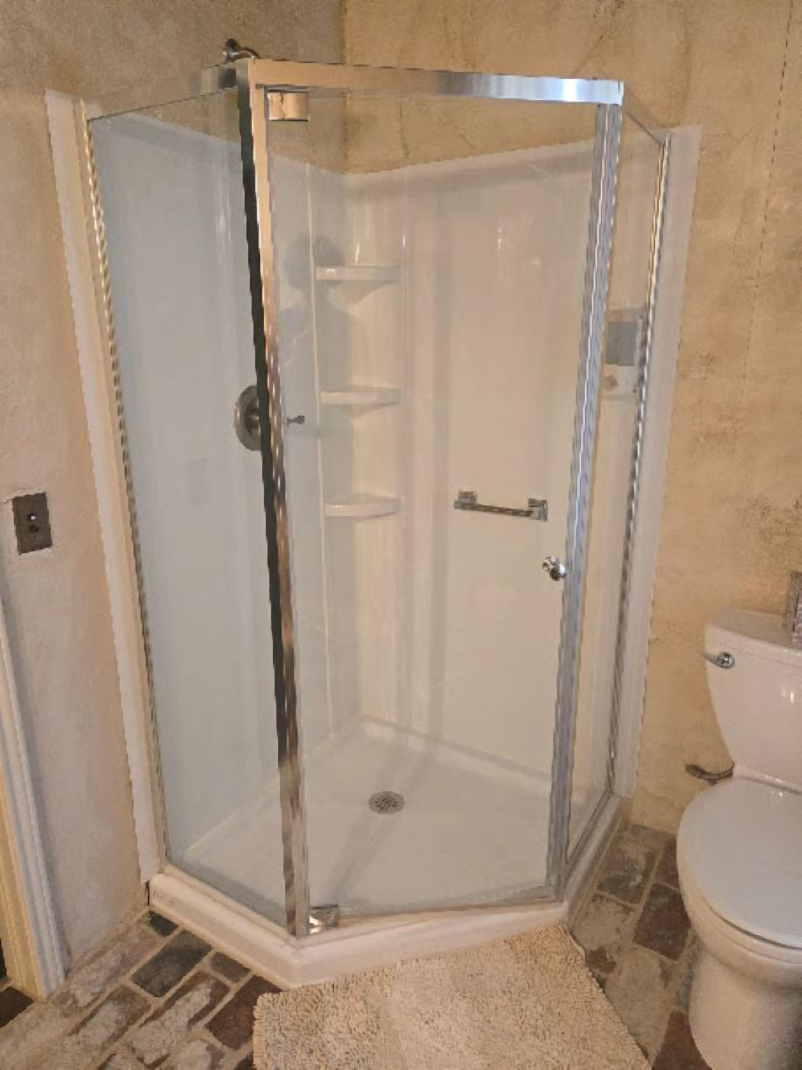 Eine gläserne Duschkabine mit hellem Boden, einer weißen Toilette und einer beige farbenen Wand.