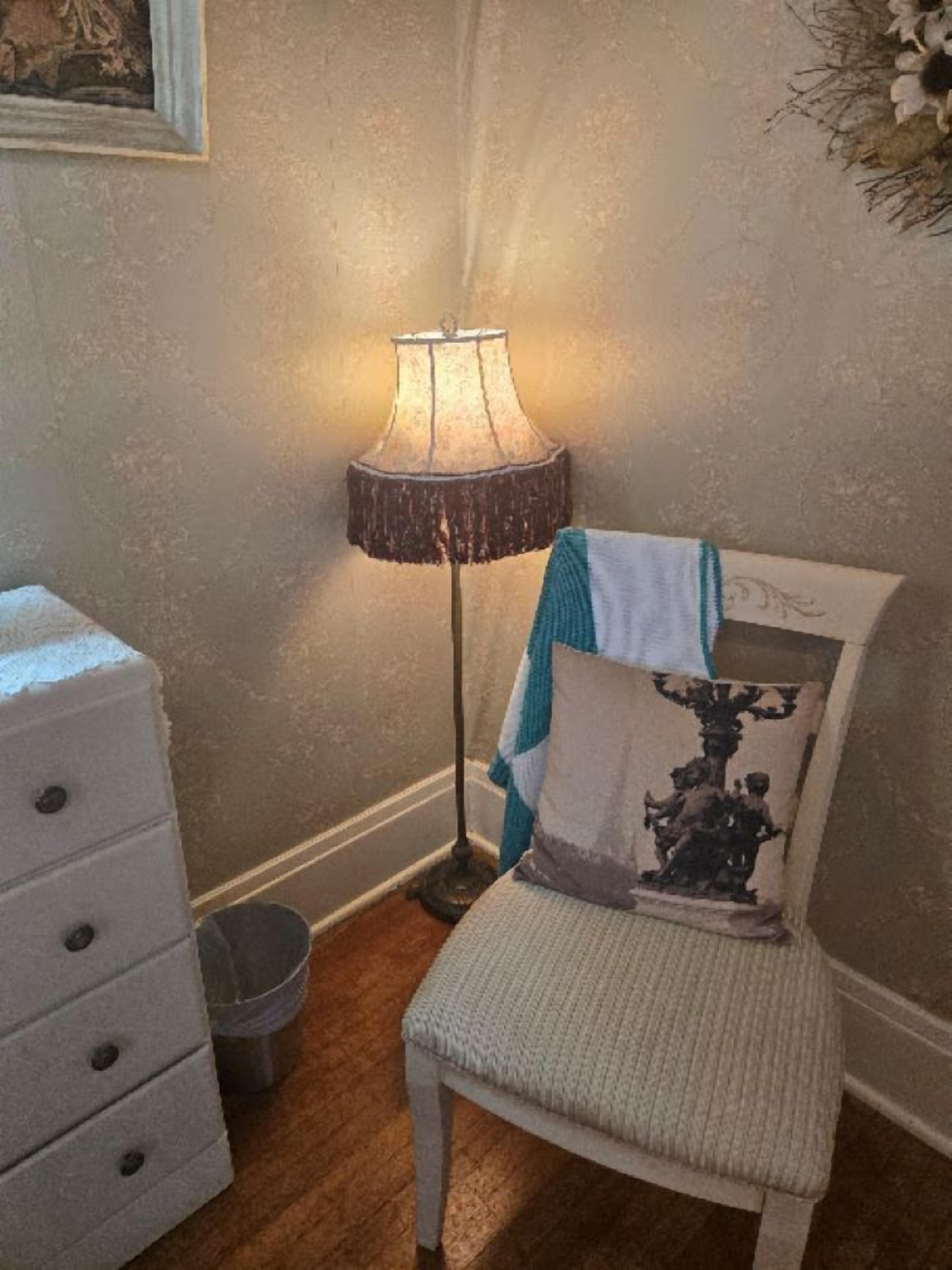Quarto com cadeira branca, luminária de chão, penteadeira branca e uma pequena lixeira.
