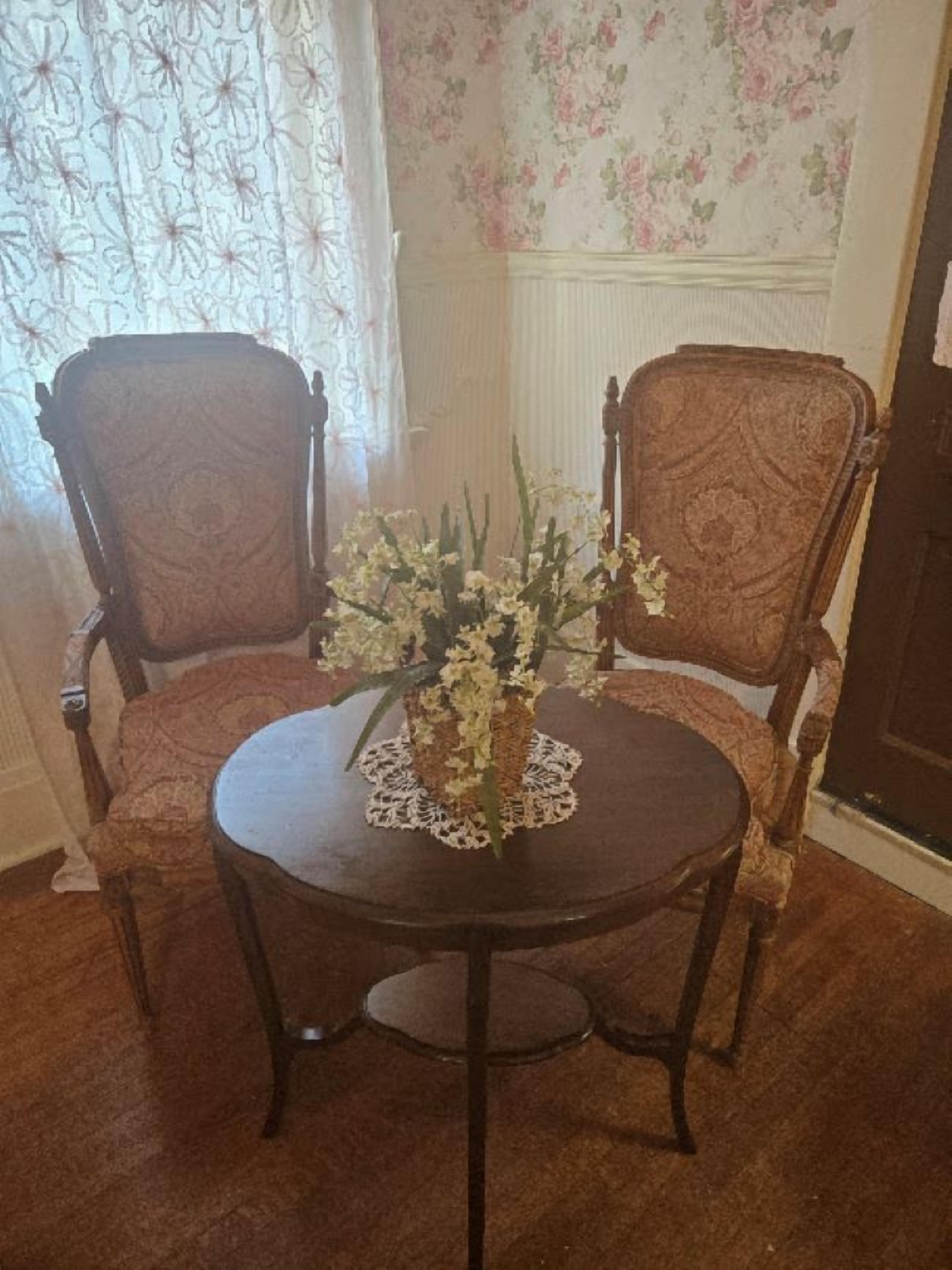 A dining table with two chairs, a lace doily, and a floral arrangement.