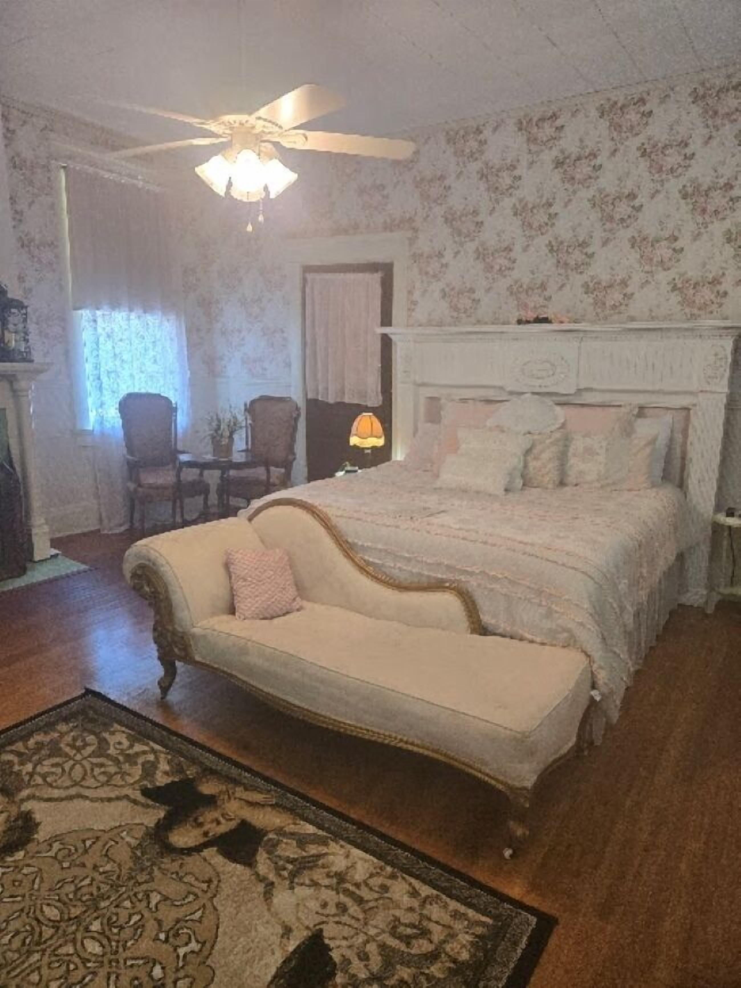 A bedroom with a bed, a chair, a lamp, and a ceiling fan.