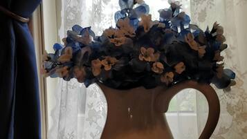 A vase with blue and white flowers on a table near a window with lace curtains.