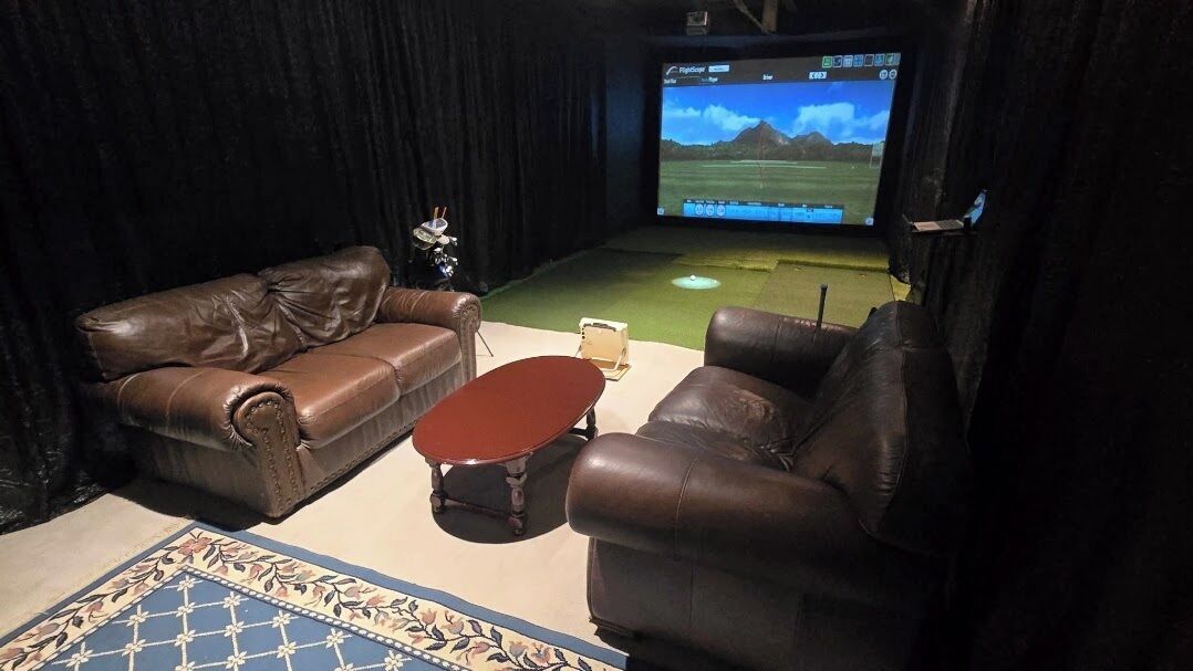 Ett hemmabiosystem med lädersoffor, ett soffbord och en stor skärm som visar en golfmatch.