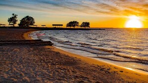 A beach with a sunset, waves, and a few trees and structures in the distance. - The Lancaster Manor B&B (Gainesville)