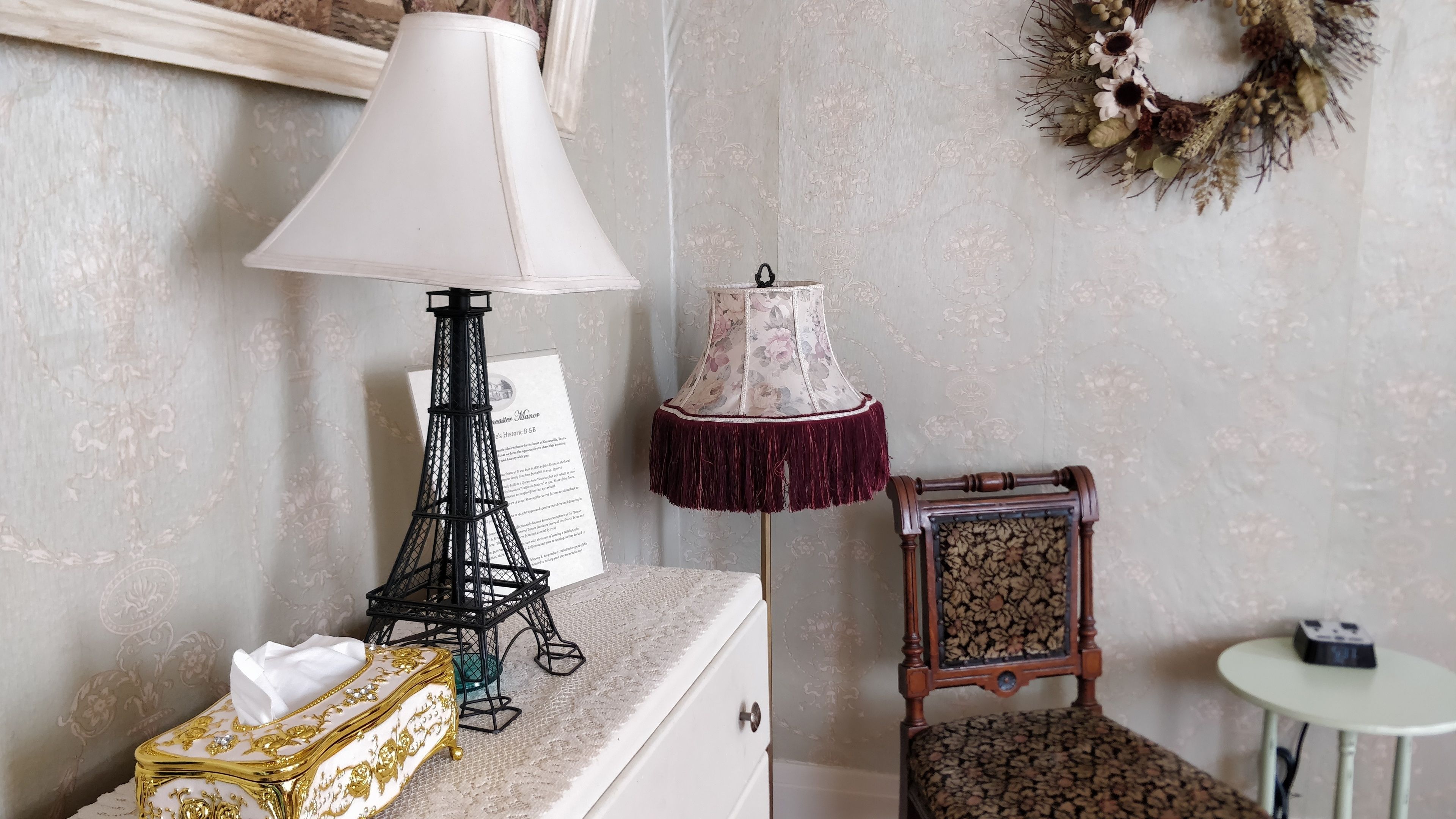 A room with a decorative lamp, a small table with a device, and a chair with a floral cushion.