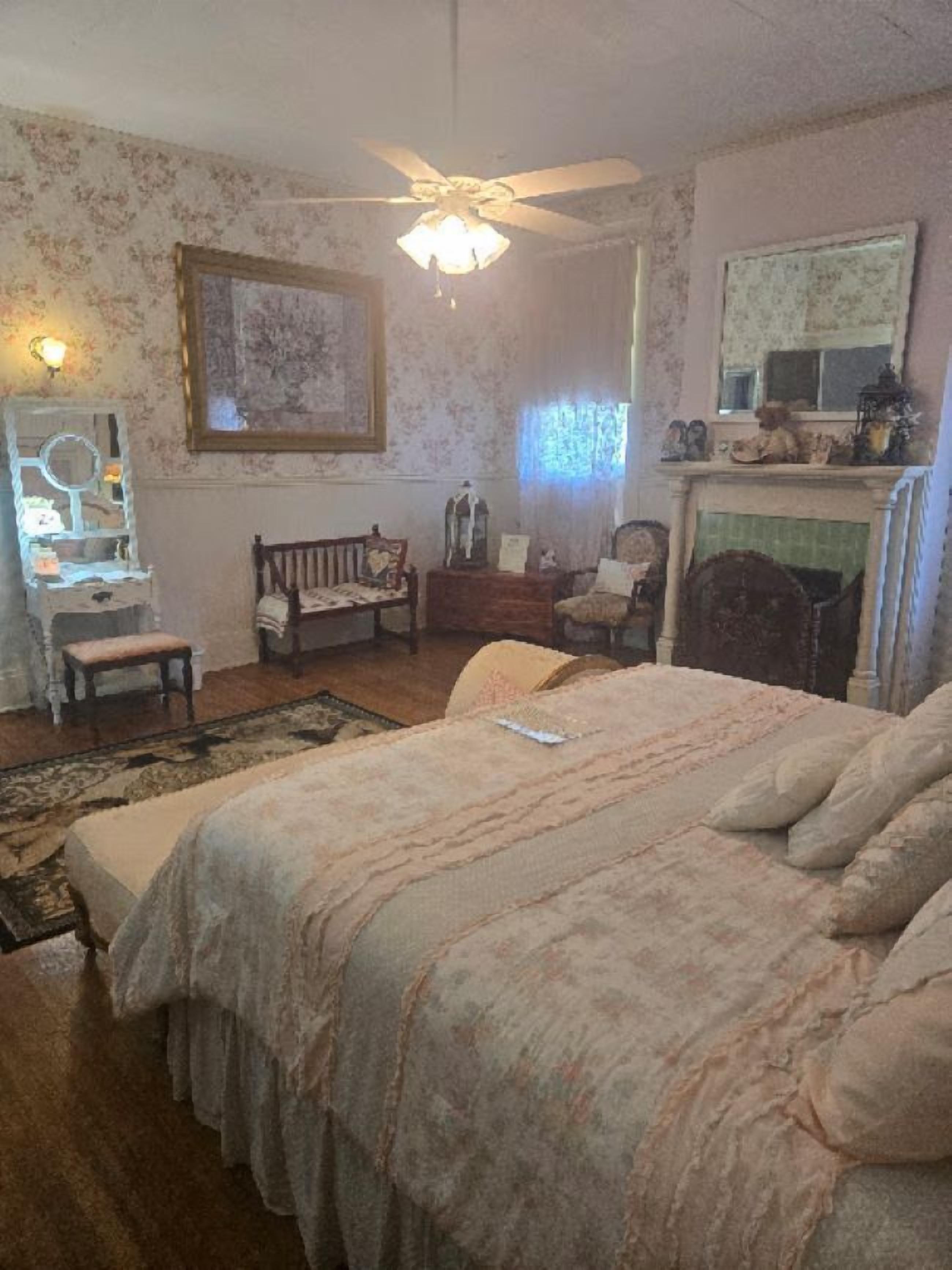 Un dormitorio con cama, una banca, cómoda, espejo y chimenea.
