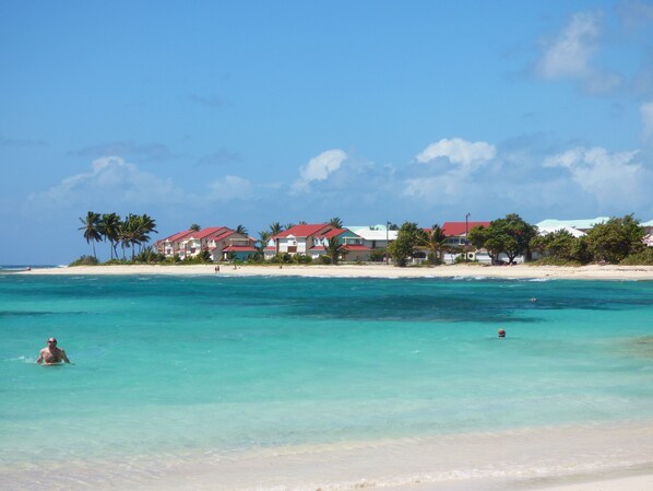Un hôtel situé en bord de mer, composé de plusieurs bâtiments aux toits rouges, avec une plage de sable fin et une eau turquoise cristalline.